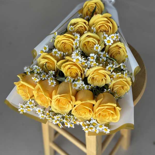 Bouquet of yellow roses with small white daisies wrapped in white paper