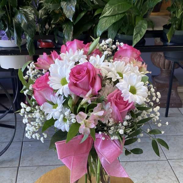 Pink roses and white daisies arranged in a glass vase with a pink ribbon