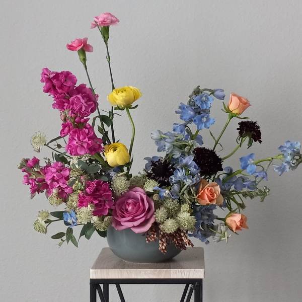 Mixed bouquet in a gray vase with pink, yellow, blue, and peach flowers