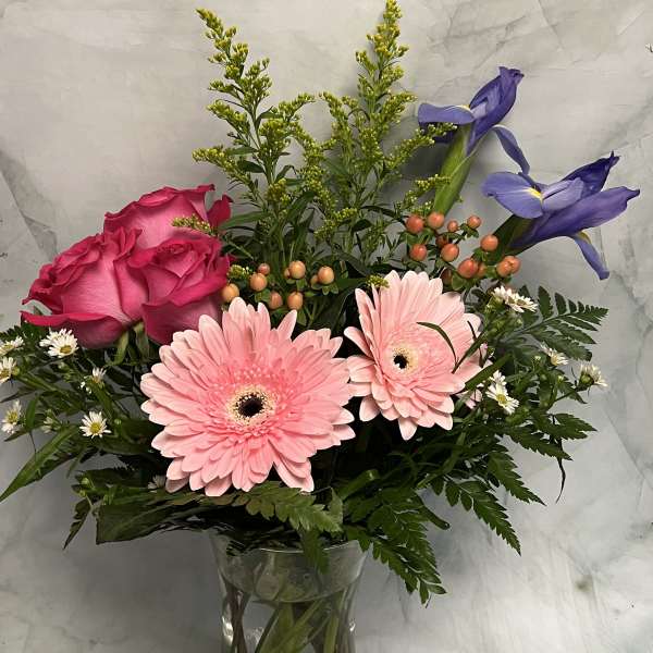 Pink roses and gerbera daisies in a clear glass vase with purple irises