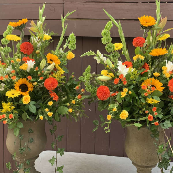 Two large floral arrangements in stone urns with orange, yellow, and white blooms