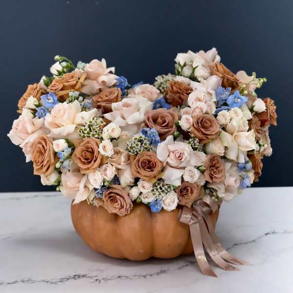 Floral arrangement in a pumpkin-shaped container with blush and tan roses