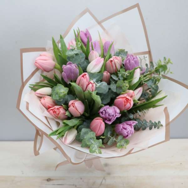 Hand-tied bouquet of pink and purple tulips with eucalyptus wrapped in white and beige paper.
