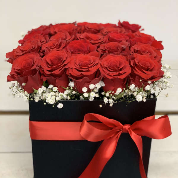 Red roses arranged in a black box with a red ribbon and white baby's breath