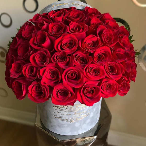 Round hatbox filled with tightly packed red roses on a reflective pedestal