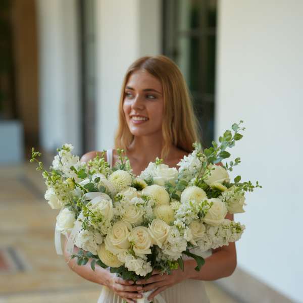 Woman holding a large white bridal bouquet with roses and round blooms