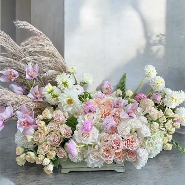 Large pastel floral arrangement with roses, orchids, and white blooms in a low container