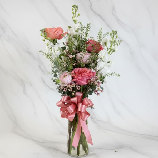Pink and white rose bouquet in a clear glass vase with a pink ribbon