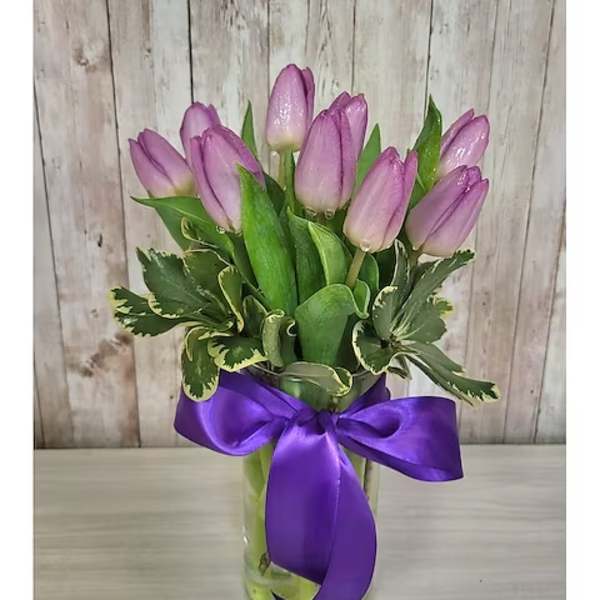 Pink tulips in a clear glass vase with a purple ribbon