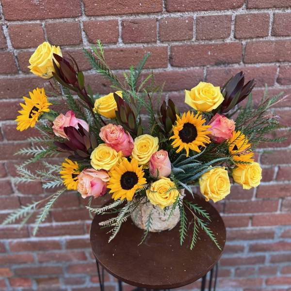 Bouquet of yellow roses and sunflowers in a textured vase