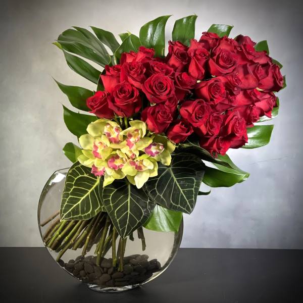 Modern arrangement of red roses and green orchids in a round glass vase with river rocks