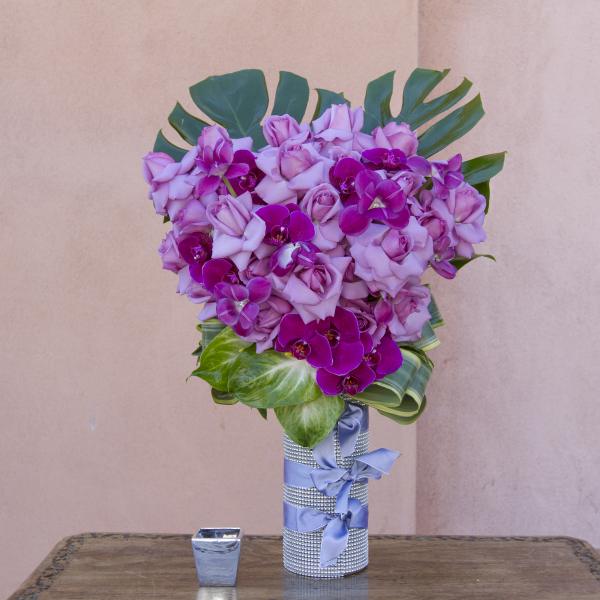 Pink roses and purple orchids arranged in a silver vase with a blue ribbon