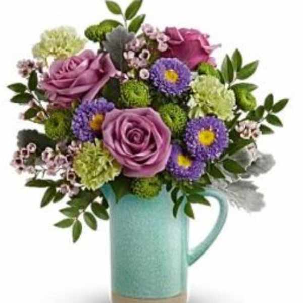 Purple roses and mixed blooms arranged in a turquoise pitcher vase
