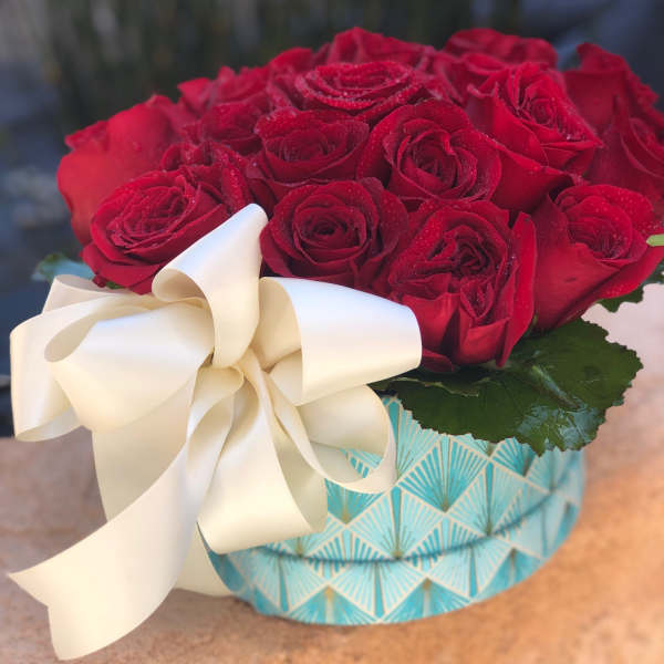 Red roses in a patterned box with a large cream ribbon