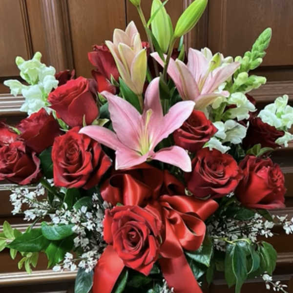 Red roses and pink lilies in a glass vase with a red ribbon