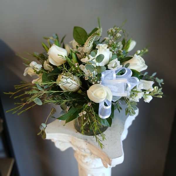 White rose bouquet in a glass vase with a white ribbon