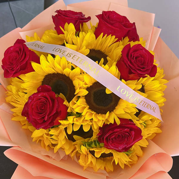 Bouquet of red roses and yellow sunflowers wrapped in peach paper