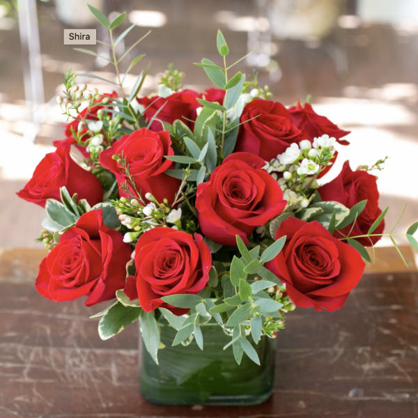 Red roses arranged in a green glass vase with white filler flowers