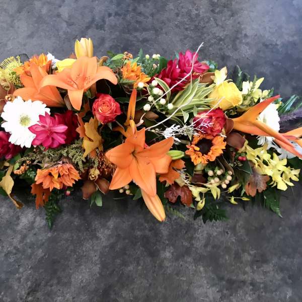 Long floral arrangement with orange lilies and mixed blooms on a dark surface