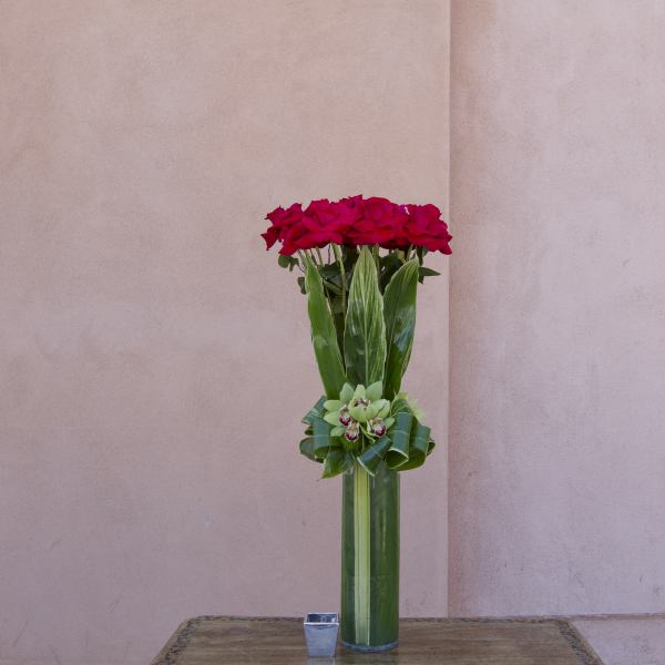 Tall vase arrangement of red roses with green orchids in a glass cylinder
