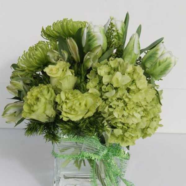 Monochromatic green arrangement of hydrangeas and mixed flowers in a clear glass cube vase with a green bow