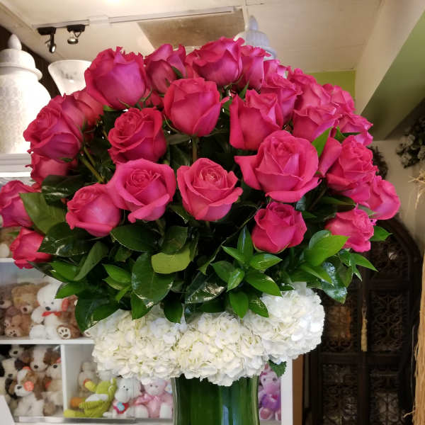 Pink roses arranged above white hydrangeas in a green glass vase
