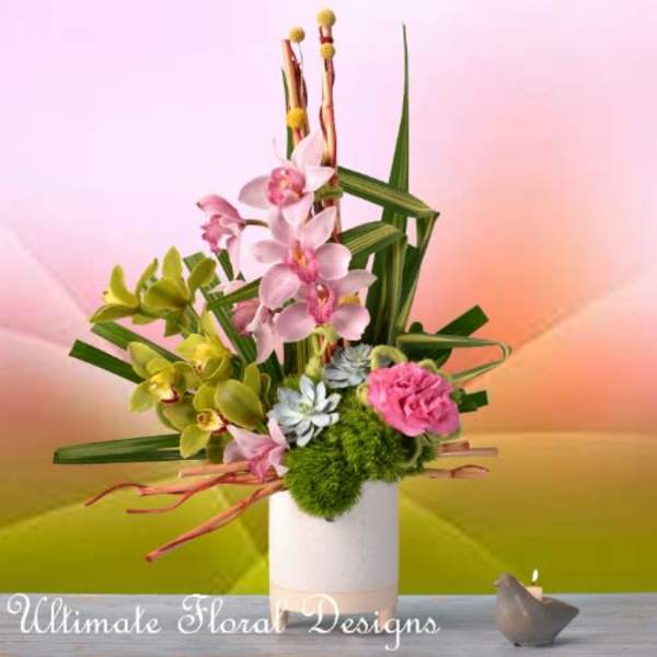 Pink and green orchid arrangement in a white vase with a small candle nearby
