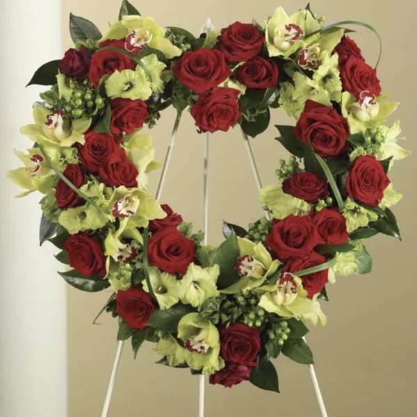 Heart-shaped wreath of red roses and green orchids on a stand