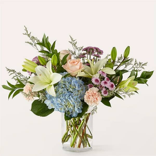 Bouquet of lilies, roses, hydrangea, and carnations in a clear glass vase