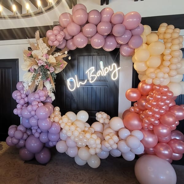 Pastel balloon arch with a floral accent and neon "Oh Baby" sign