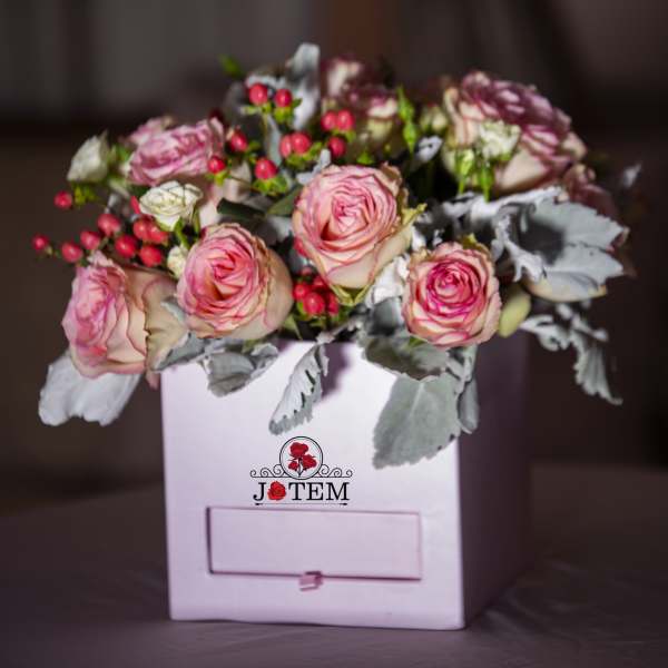 Pink roses arranged in a white box with red berry accents