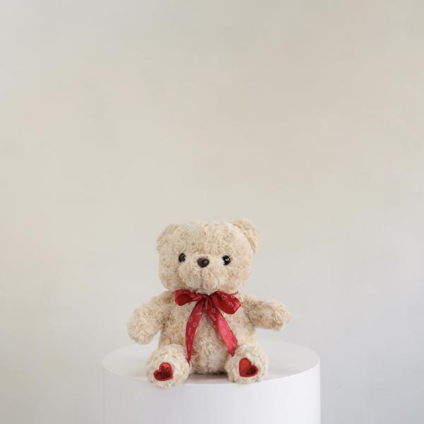 Plush teddy bear with a red ribbon sitting on a white pedestal