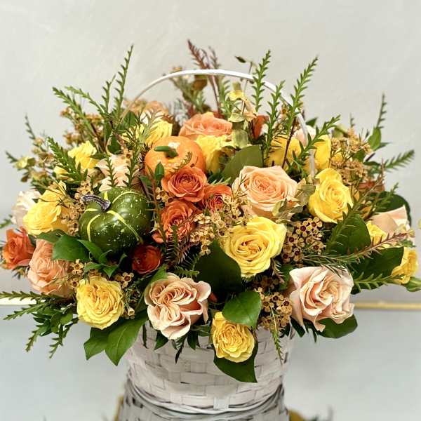 Basket arrangement of peach and yellow roses with small pumpkins