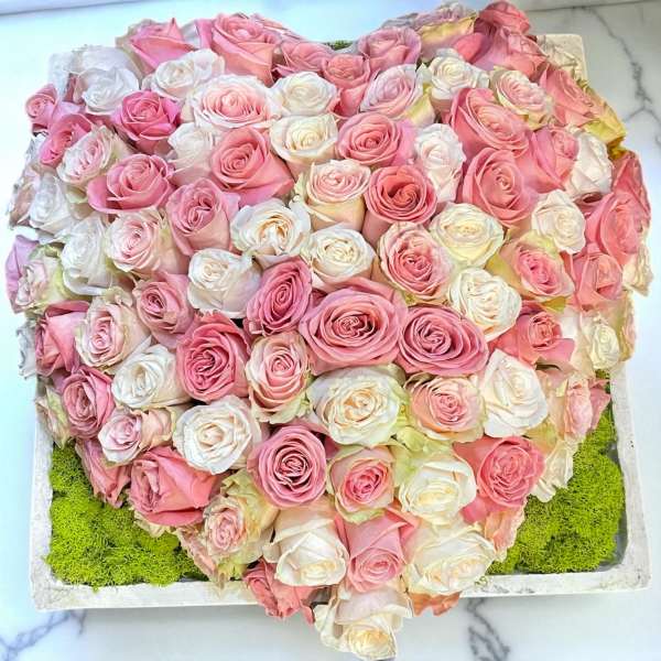 Heart-shaped arrangement of pink and white roses in a shallow box