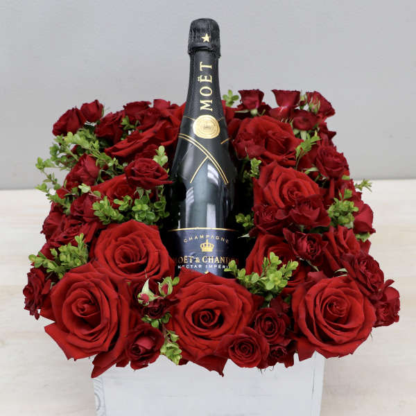 Red roses arranged around a Moët & Chandon champagne bottle in a white box
