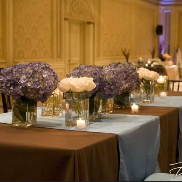 Purple hydrangea and white rose centerpieces in glass vases on a banquet table