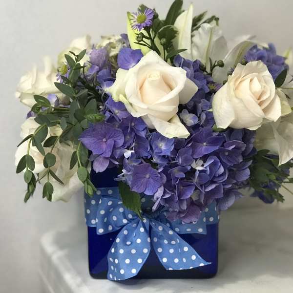 White roses and purple hydrangeas in a blue box with a polka-dot ribbon