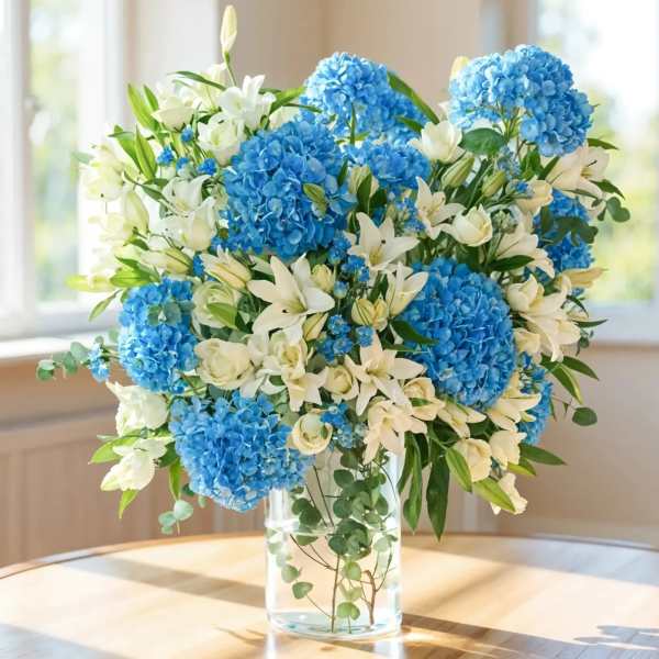 Blue hydrangeas and white lilies in a clear glass vase