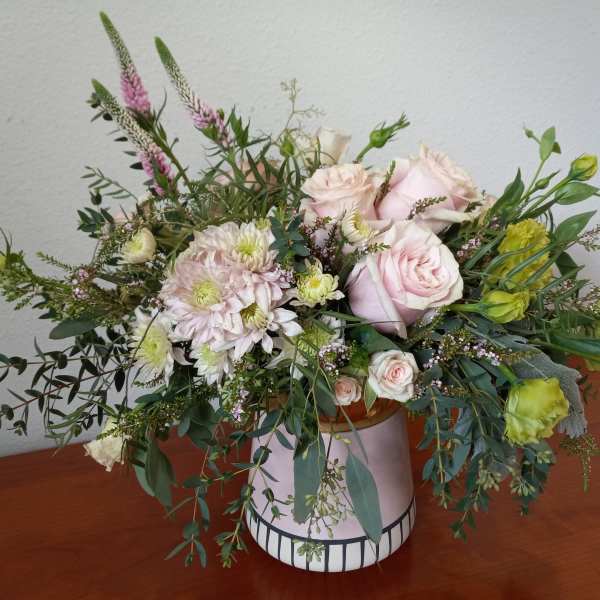 Pink roses and pale blooms arranged in a ceramic vase