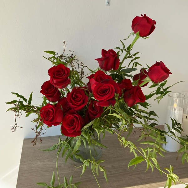 Red roses arranged in a clear glass vase with trailing greenery