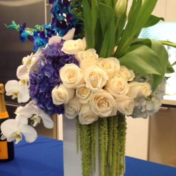 Tall floral arrangement with white roses, orchids, and blue-purple flowers in a white vase