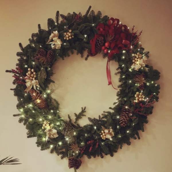 Decorated evergreen wreath with lights, pinecones, bows, and red accents