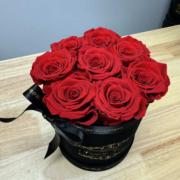 Round black hat box filled with tightly packed red roses on a light wood table