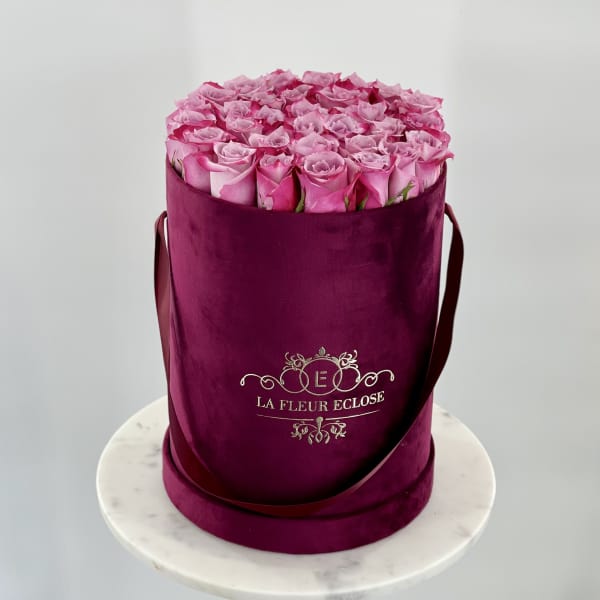 Pink roses arranged in a tall velvet hatbox with ribbon handles