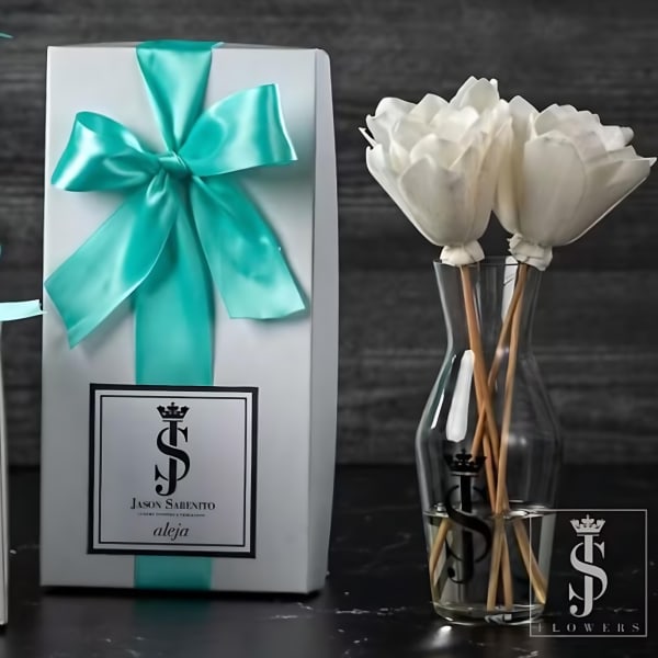 White flowers in a clear glass vase beside a gift box with a teal ribbon.