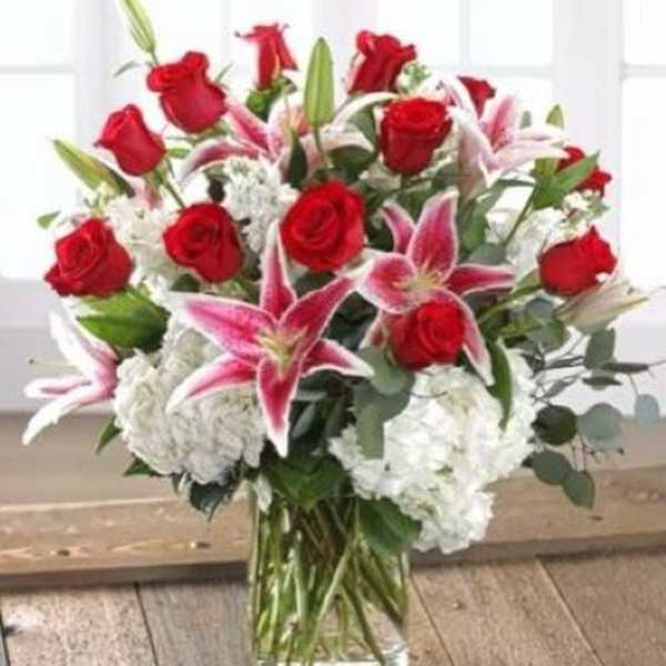 Arrangement of red roses, pink lilies, and white hydrangeas in a clear glass vase