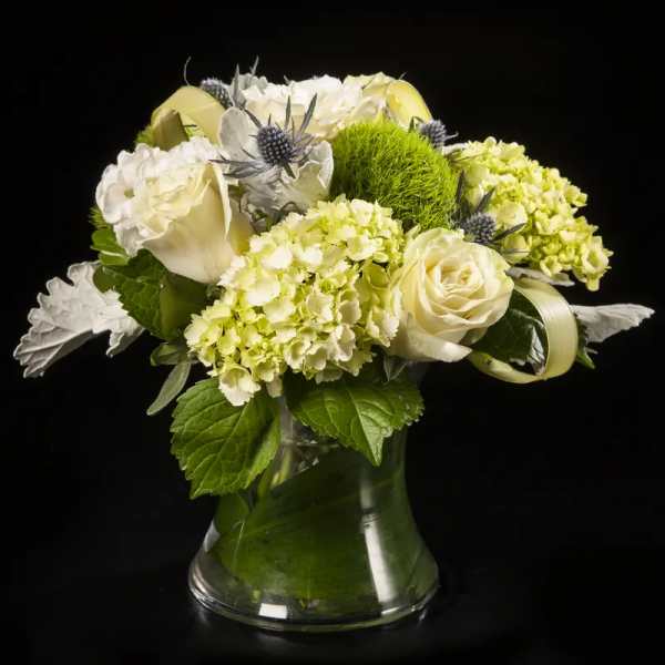 White roses and pale green hydrangeas in a clear glass vase