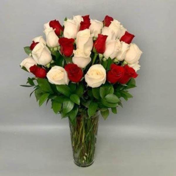 Tall clear vase filled with red and white roses in a rounded arrangement