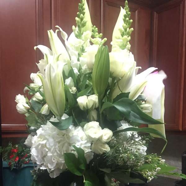 Tall arrangement of white lilies, roses, snapdragons, and hydrangeas in a clear glass vase