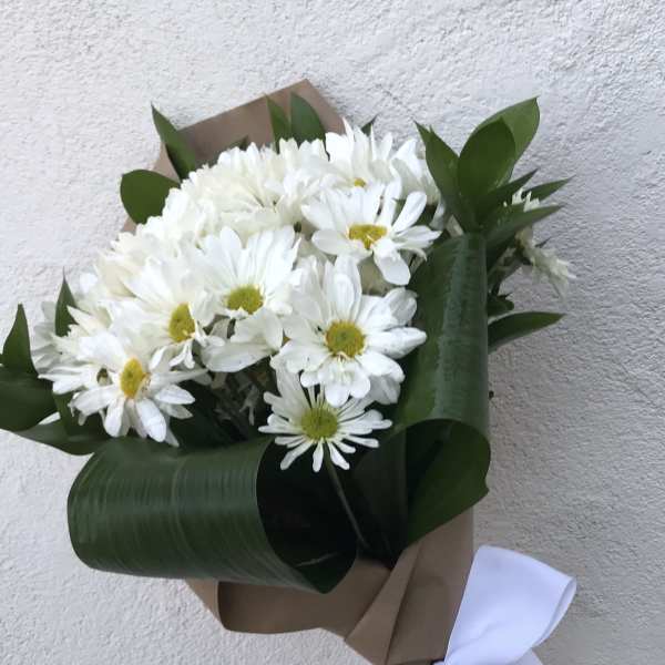 Bouquet of white daisies wrapped in brown paper with a white ribbon